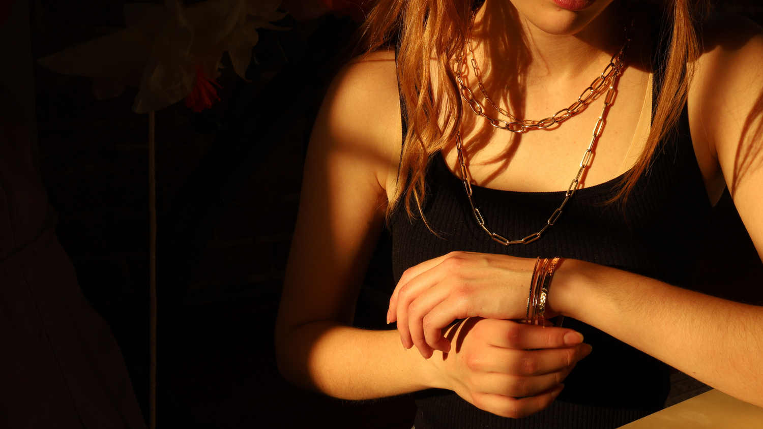 Person wearing a black sleeveless top and gold chain necklace with a blurred background